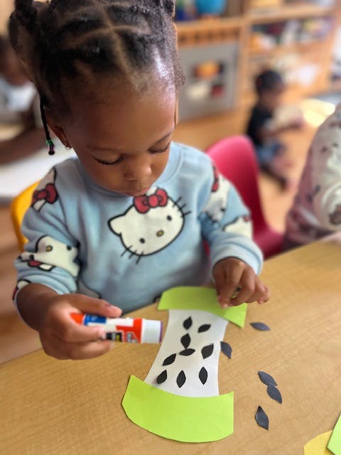Child gluing paper cutouts onto a craft project
