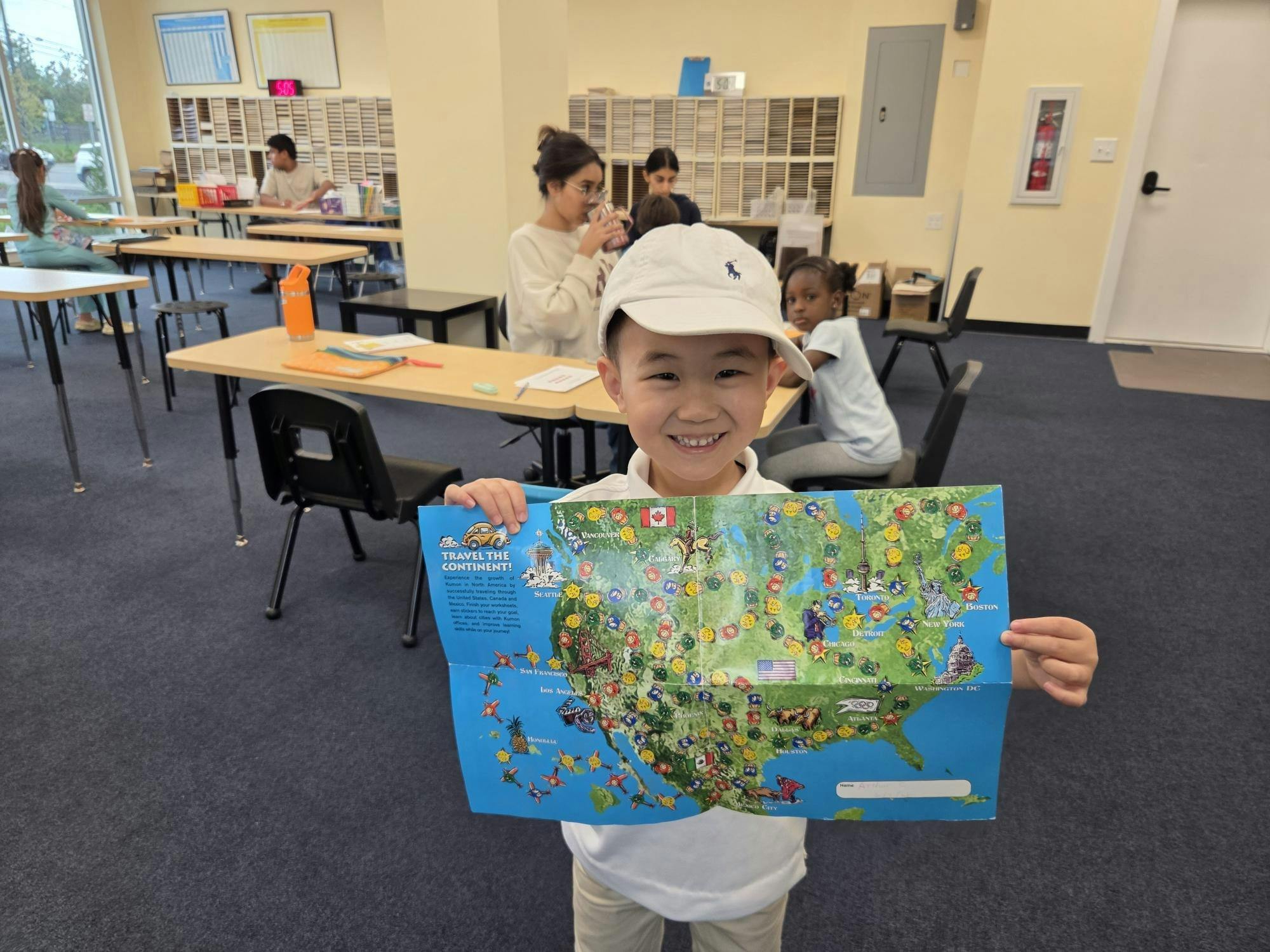 Child in a classroom holding up a map with "Travel the Continent!" written on it