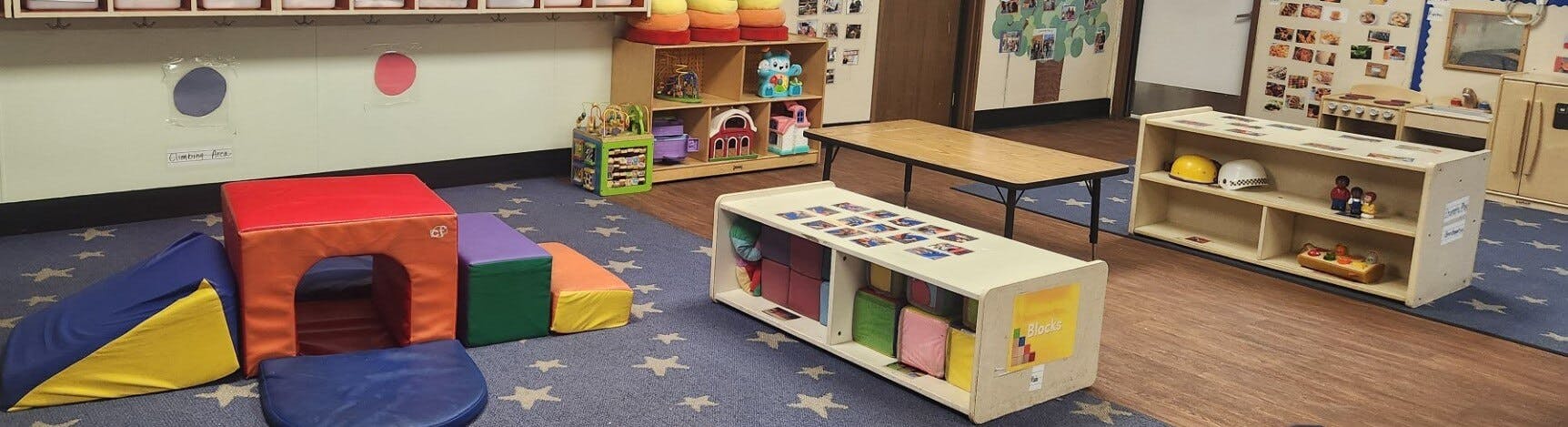 A classroom with play equipment, shelves, and a table on star-patterned carpet