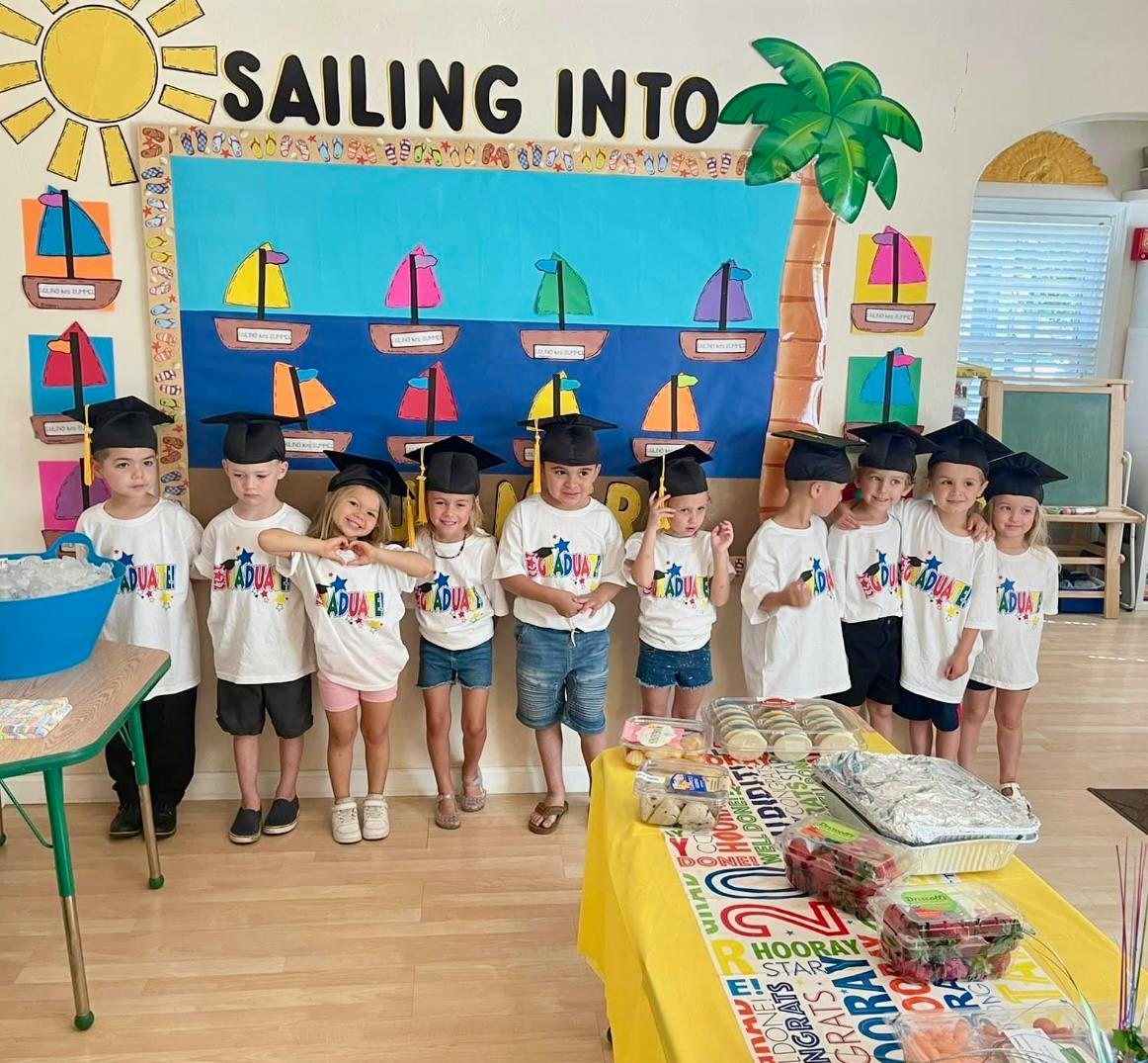Children in graduation caps standing in a classroom with a "Sailing Into" sign