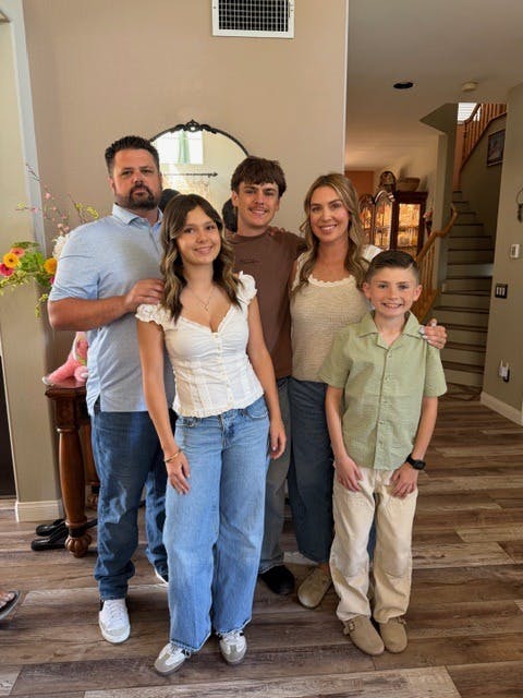 Group of two adults and three children standing together indoors