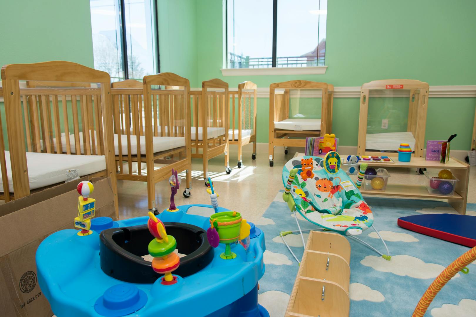 Nursery room with multiple cribs and baby play items