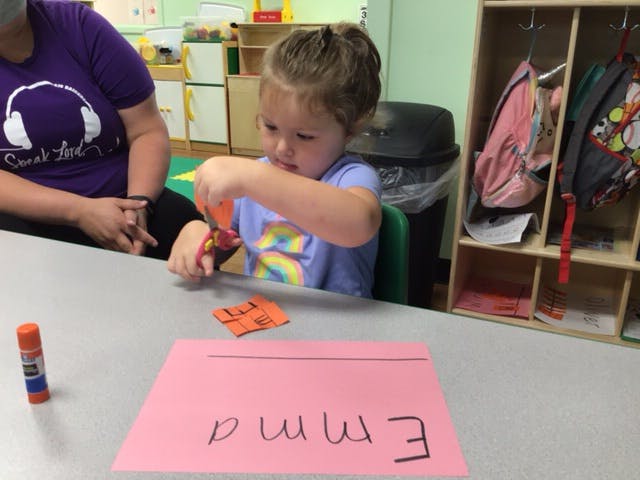 Child cutting orange paper with scissors at a table