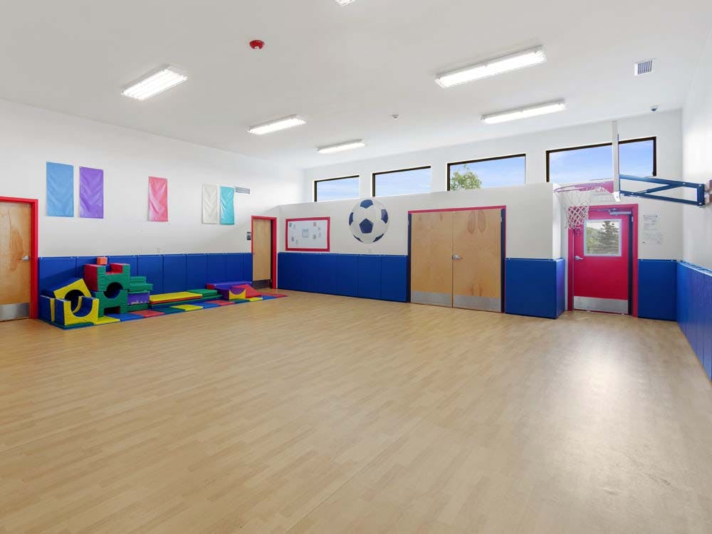 Indoor play area with soft colorful play equipment and a basketball hoop