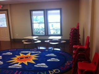 Classroom with a sun rug, small tables, and stacked red chairs