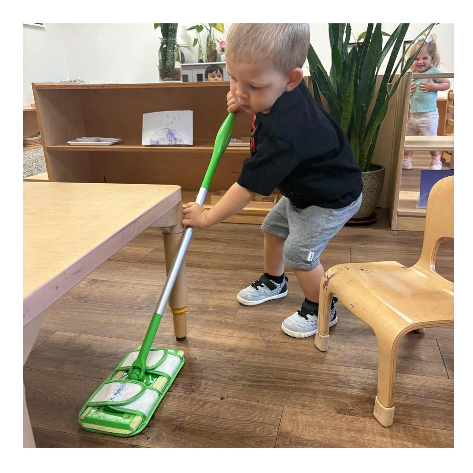 Child using a small mop on a classroom floor