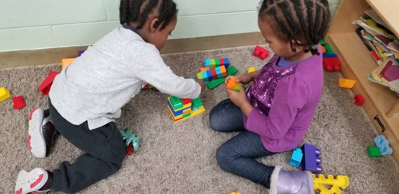 Two children playing with colorful building blocks on a carpeted floor