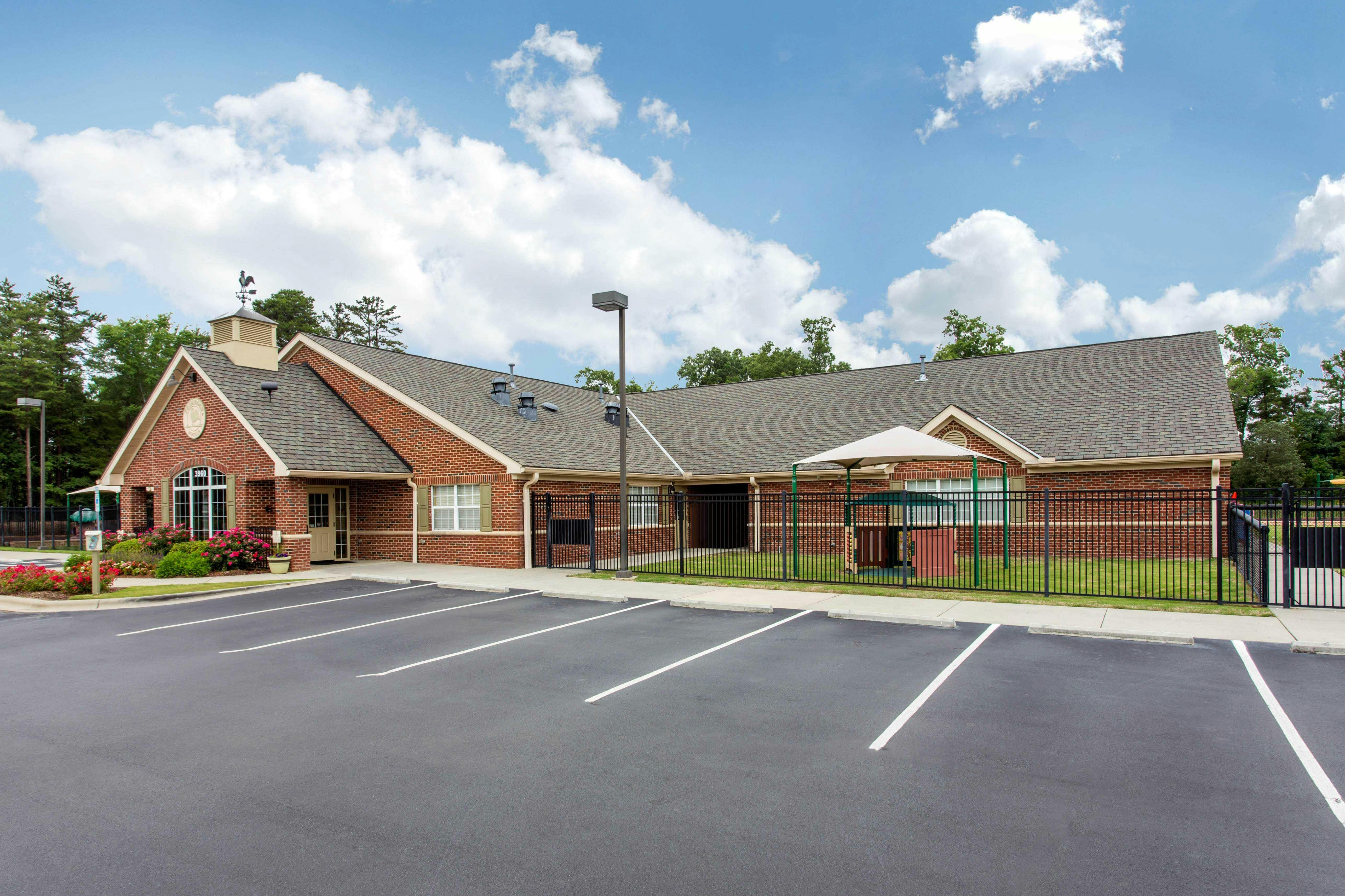 Brick building with a parking lot in front and a fenced play area
