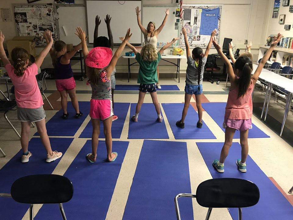 Adult and children with arms raised in a classroom
