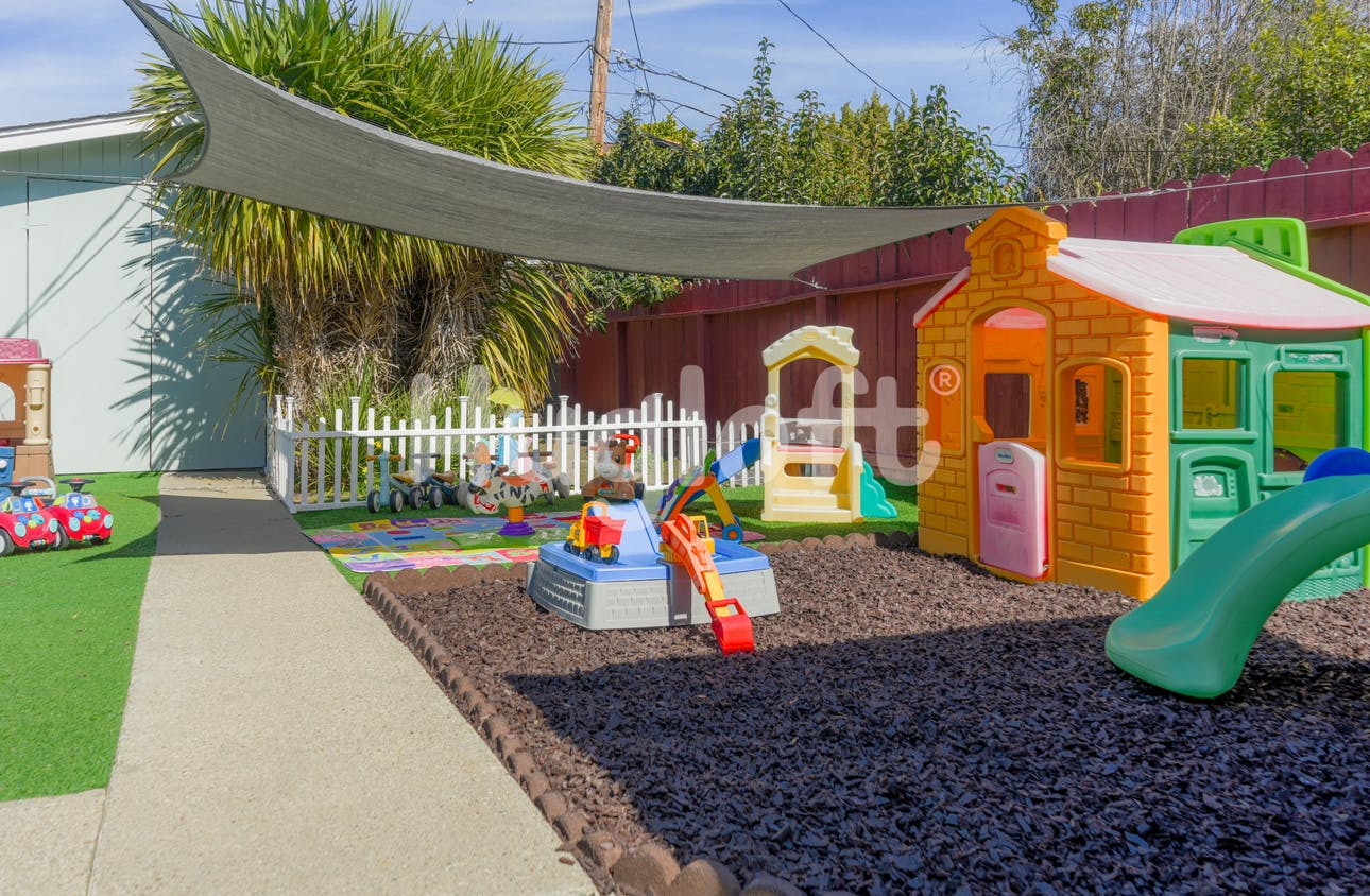 Outdoor playground with playhouses, slides, and a white picket fence