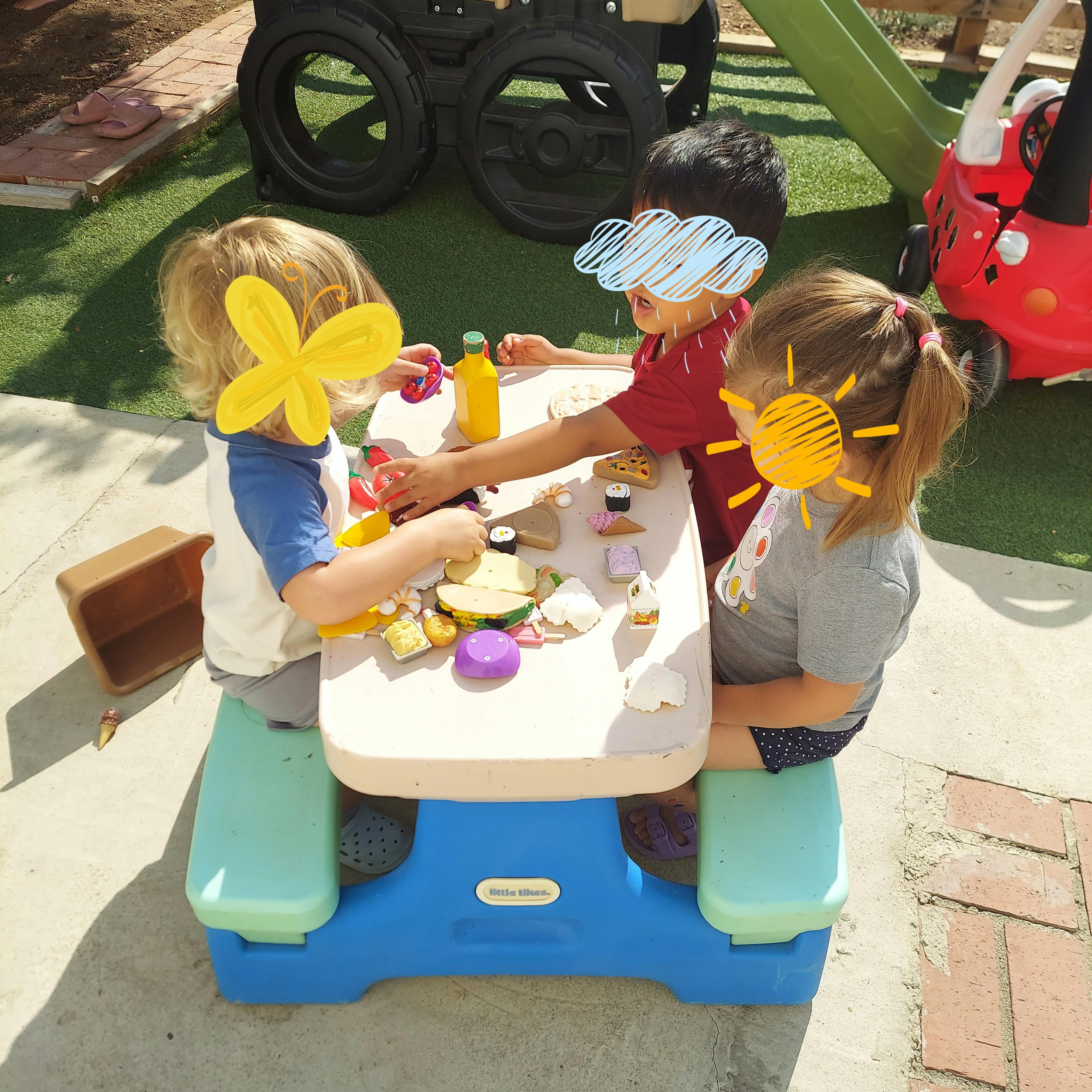 Three children playing at a small table outdoors