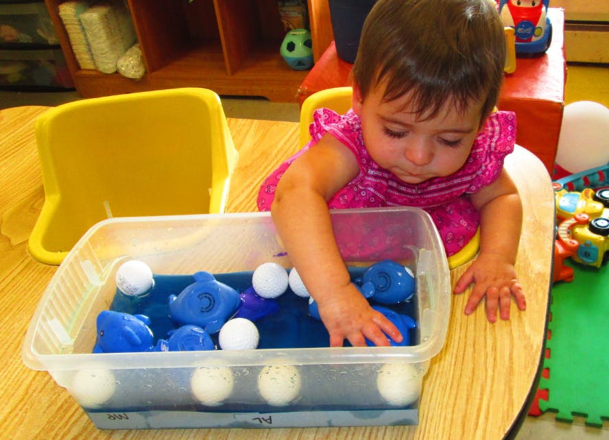 Child playing with blue toys and white balls in a clear bin of water