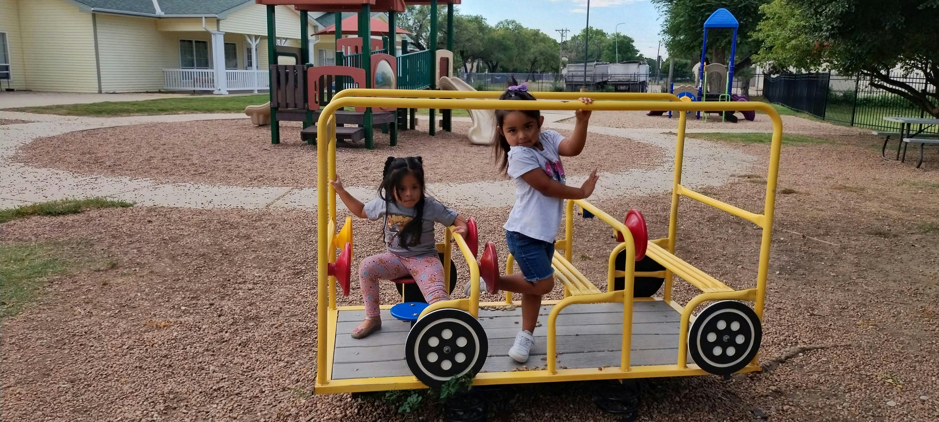 Two children playing on a metal vehicle structure at a playground