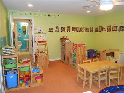 Playroom with small wooden tables and chairs, shelves with toys, and a bathroom