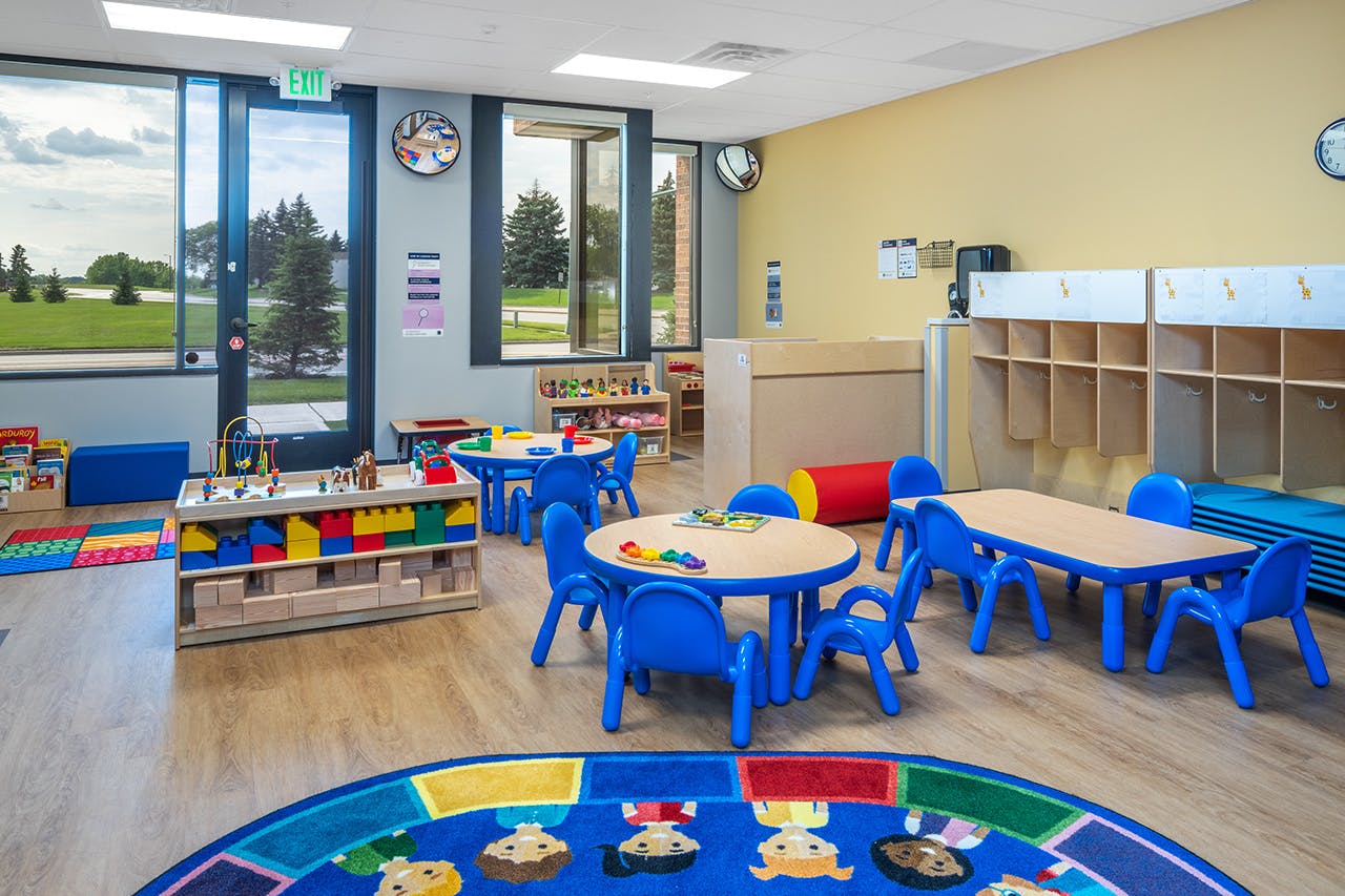 Preschool classroom with small tables and chairs, cubbies, and large windows