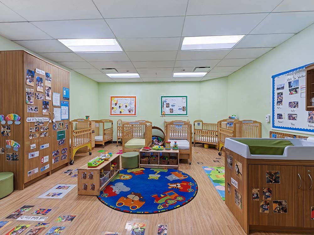Room with several cribs, a changing station, and play mats on the floor