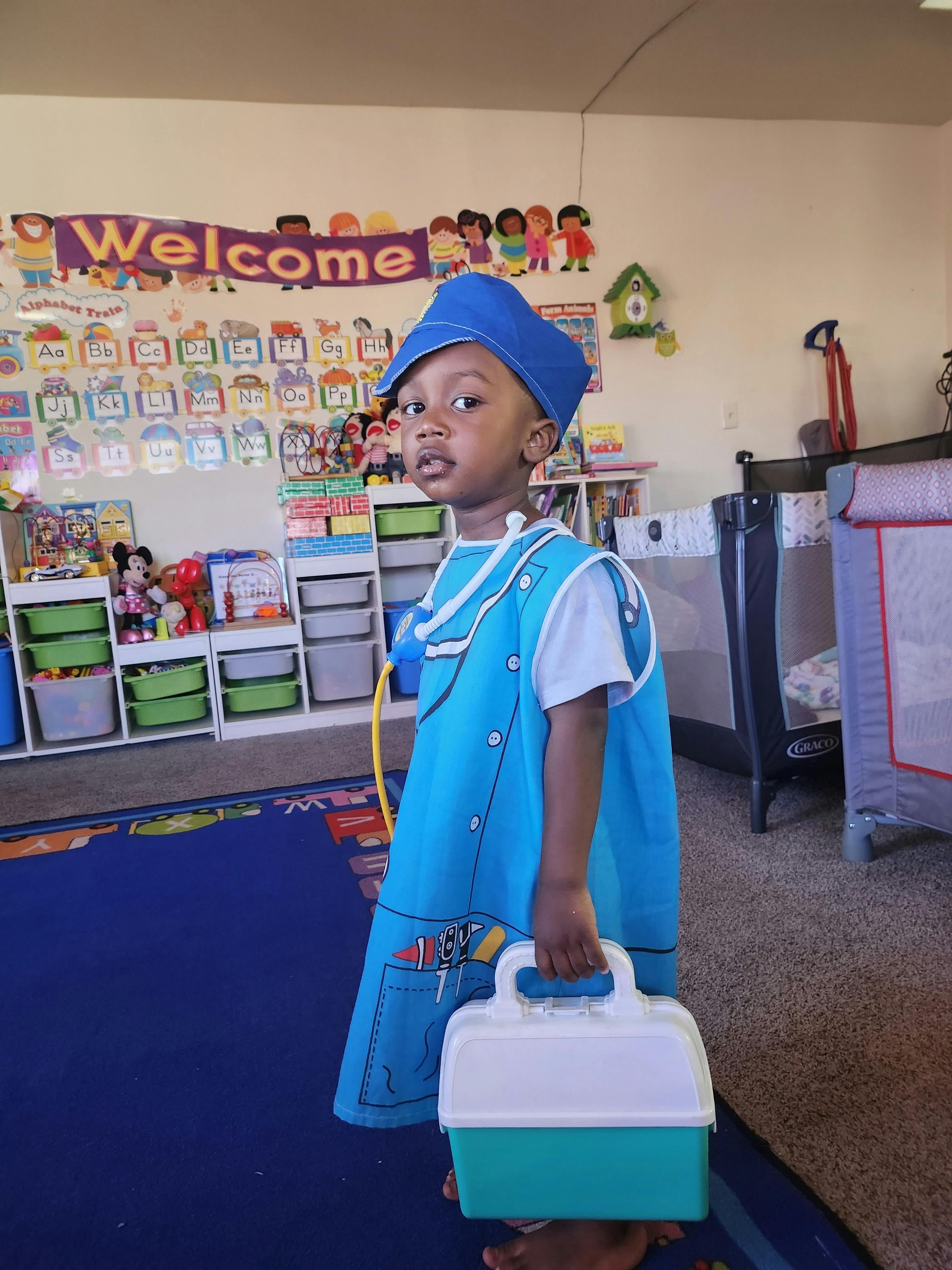 Child in a blue costume and hat holding a small box in a classroom