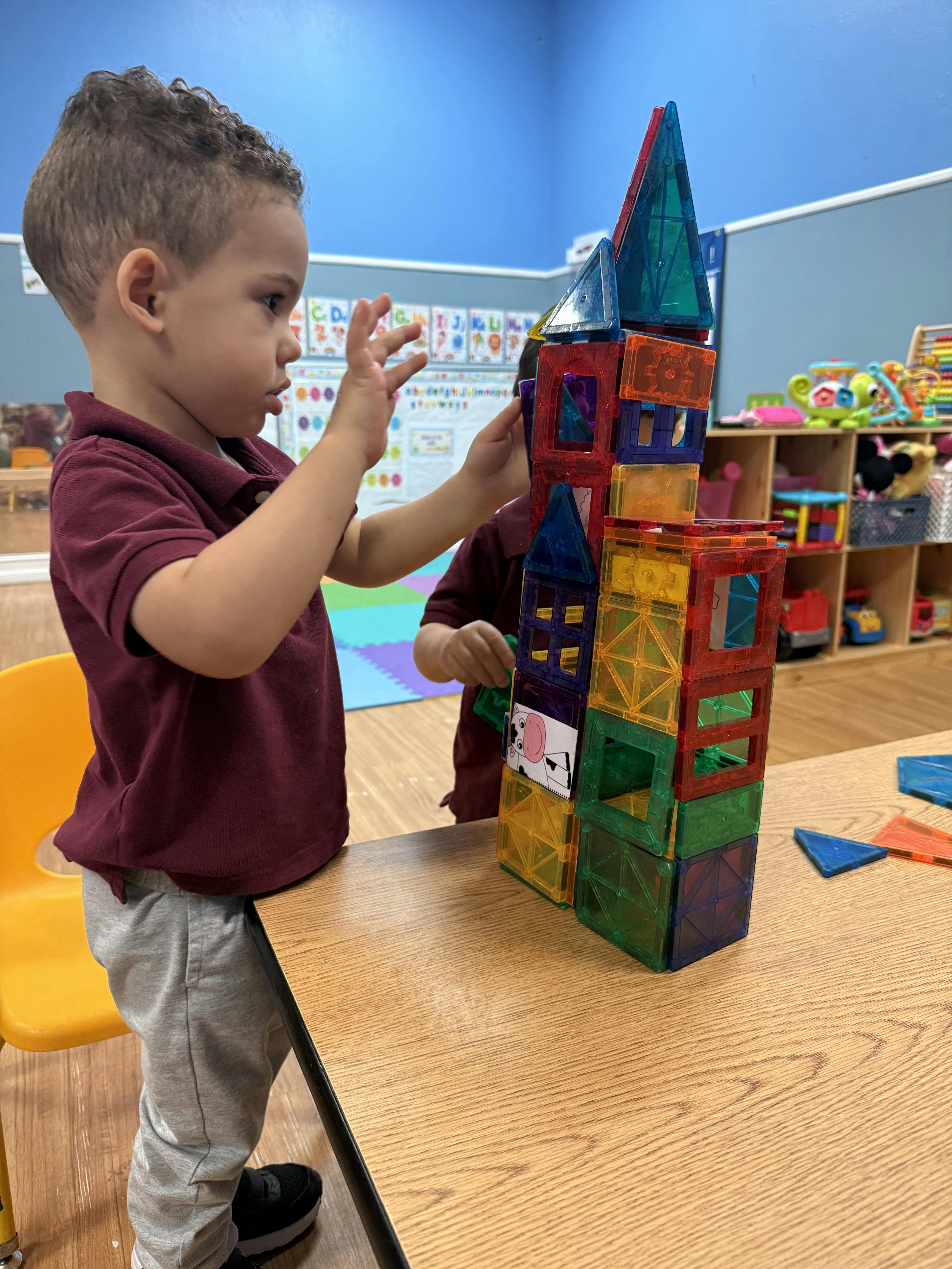 Child building a tall structure with colorful magnetic tiles in a classroom