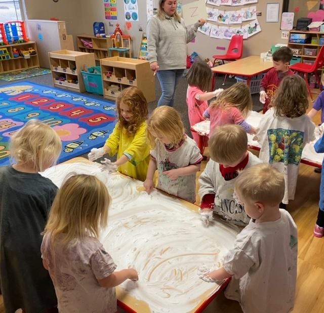 Children playing with shaving cream on a table in a classroom