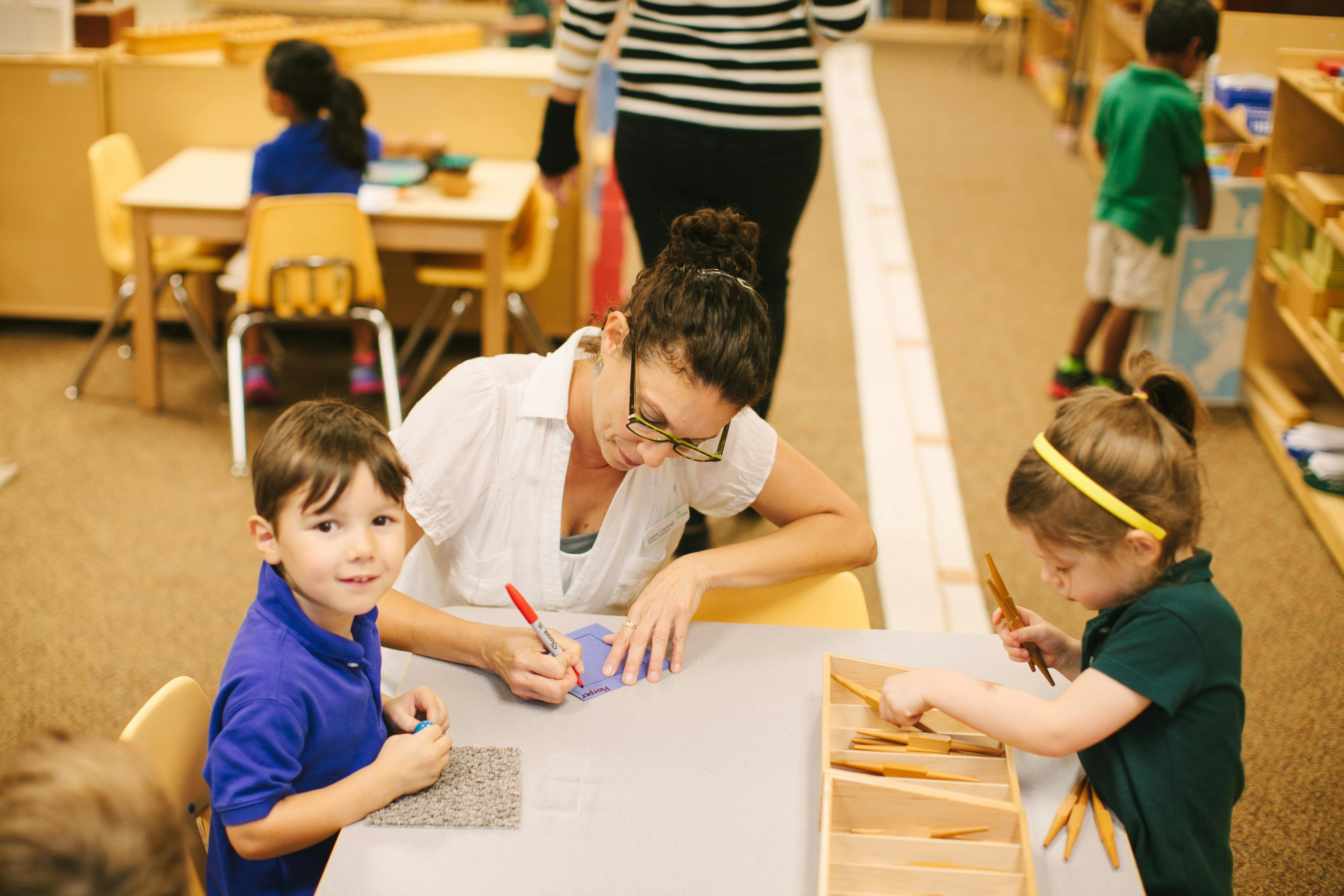 Adult and two children working at a table in a classroom