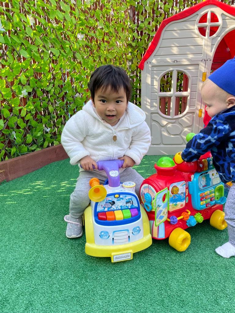 Child on a ride-on toy next to another child and toy train
