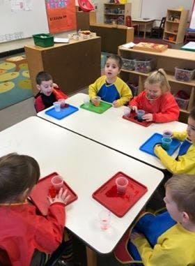 Children at tables with cups and trays in a classroom