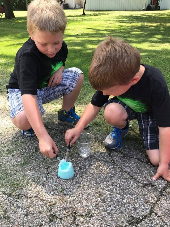 Two children crouching and experimenting with a blue substance outdoors