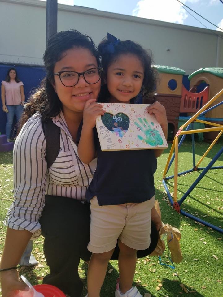 Person and child holding up a drawing with a heart and handprint