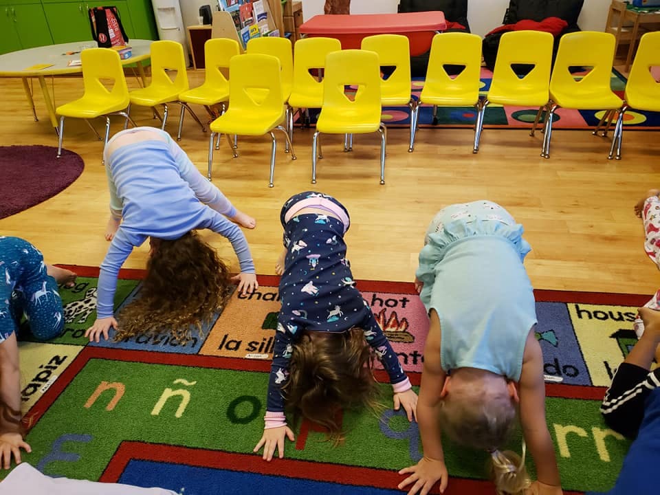 Three children doing downward dog yoga pose on a colorful rug