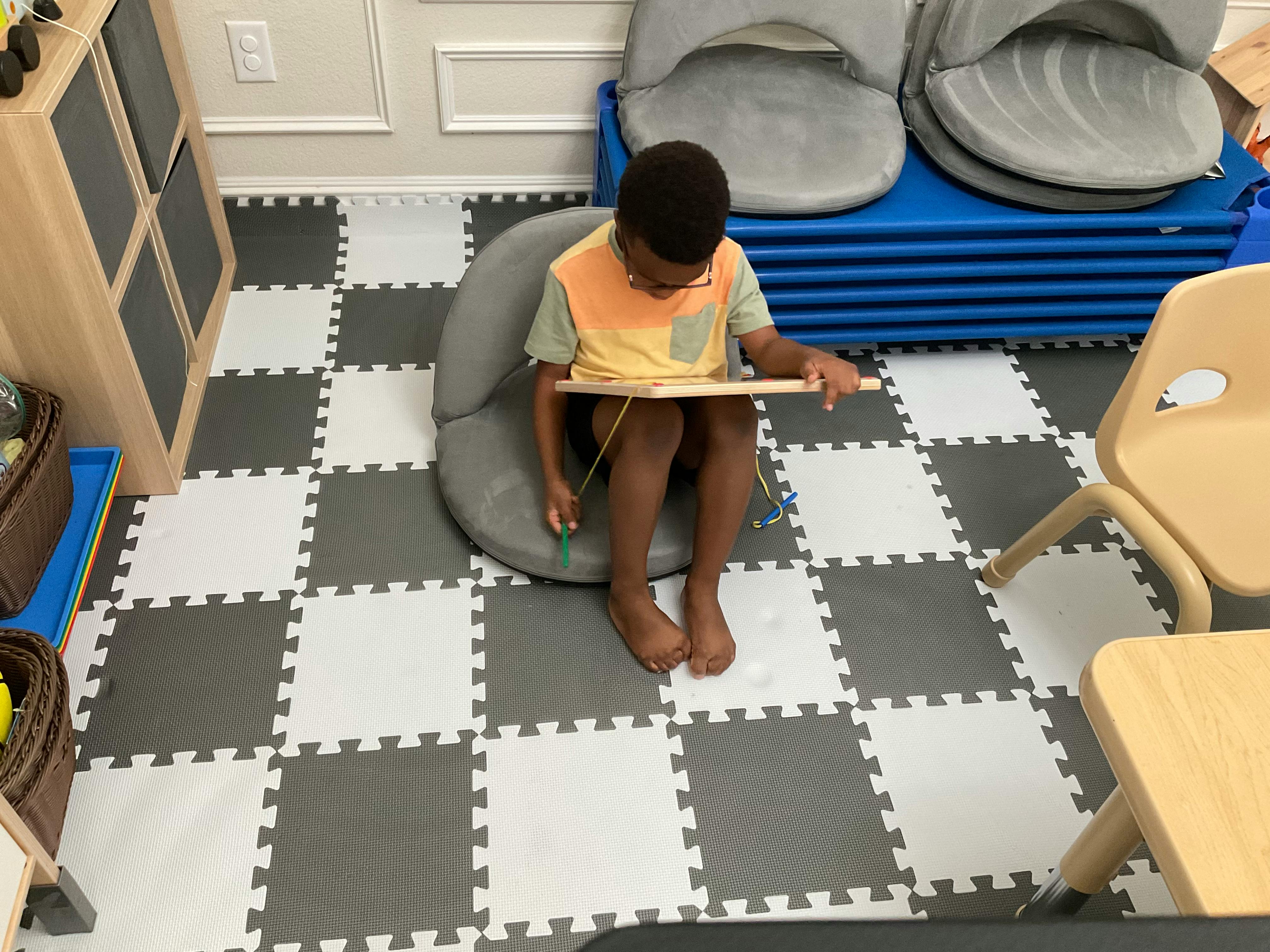 Child sitting on floor cushion with a board on lap