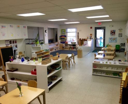 Classroom with small tables and chairs, shelves with learning materials
