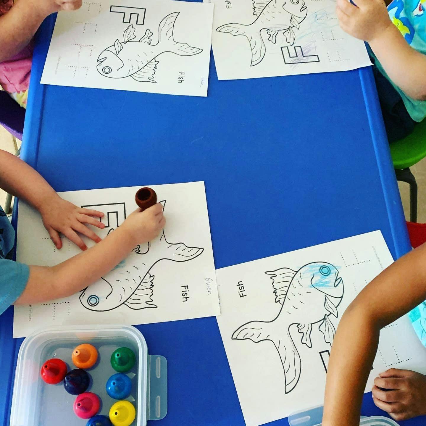 Children coloring fish drawings at a blue table