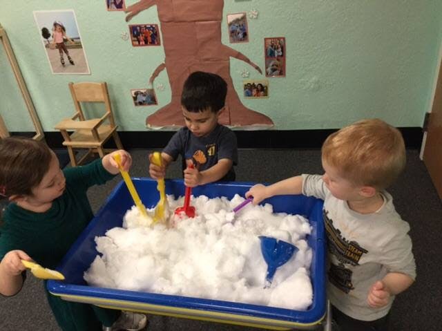Three children playing with white foam in a blue bin