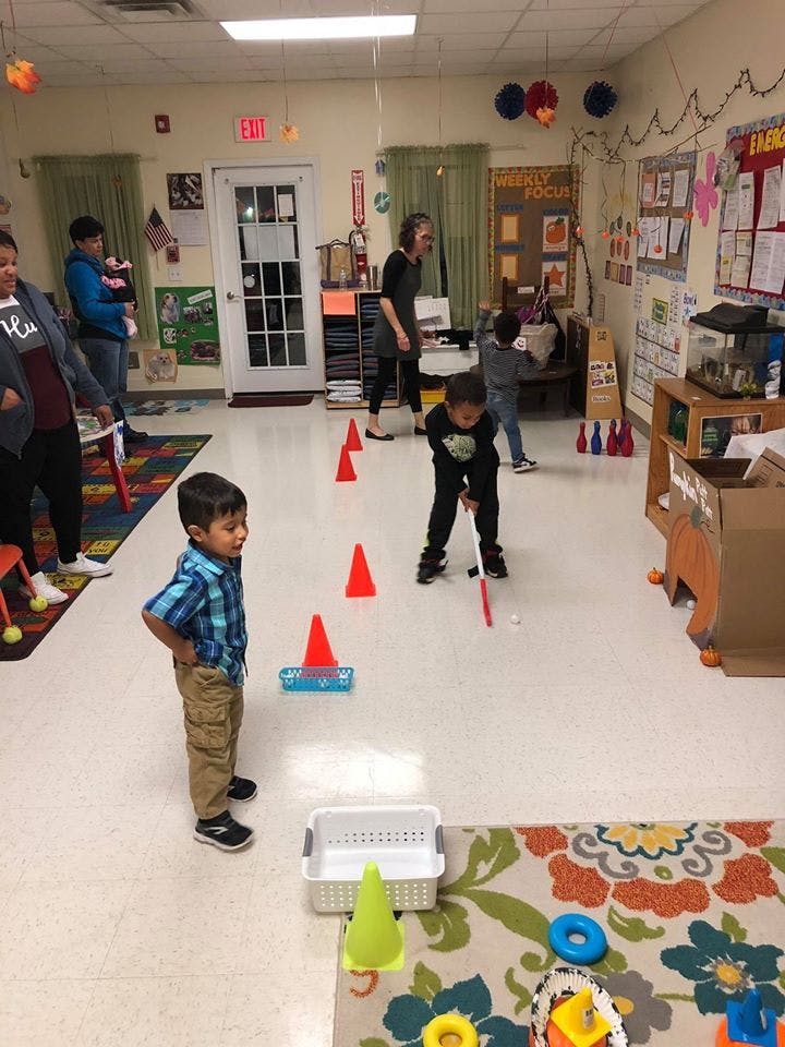 Children and adults in a room with one child playing mini golf