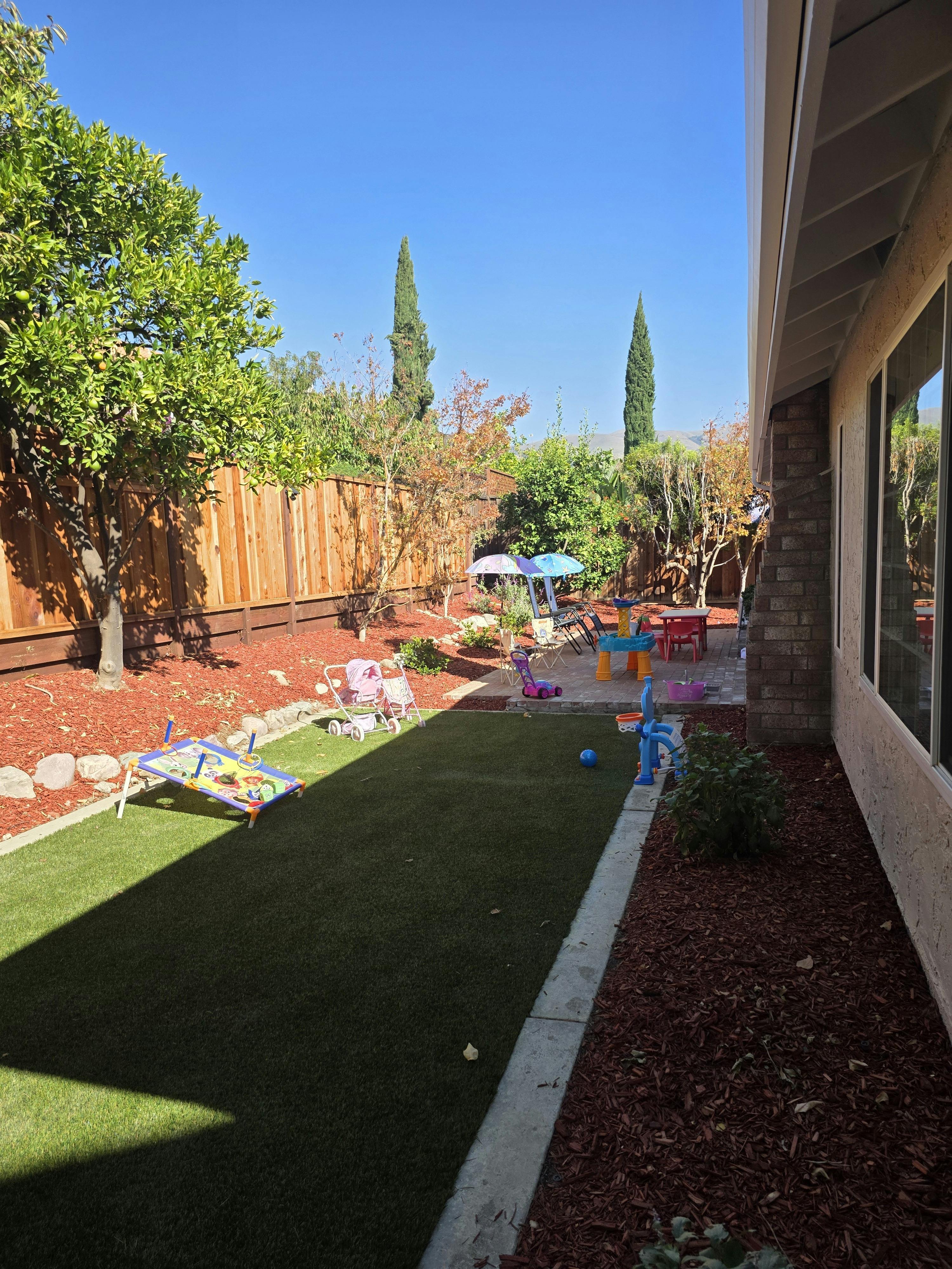 Backyard with artificial turf, wood chip landscaping, and children's play items