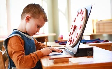 Child writing at a desk with a clock model