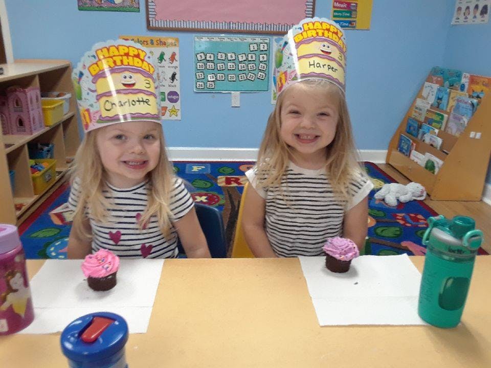 Two children wearing birthday hats sitting at a table with cupcakes