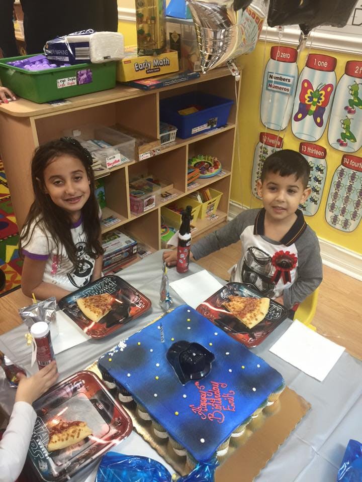 Two children sitting at a table with pizza and a blue cake