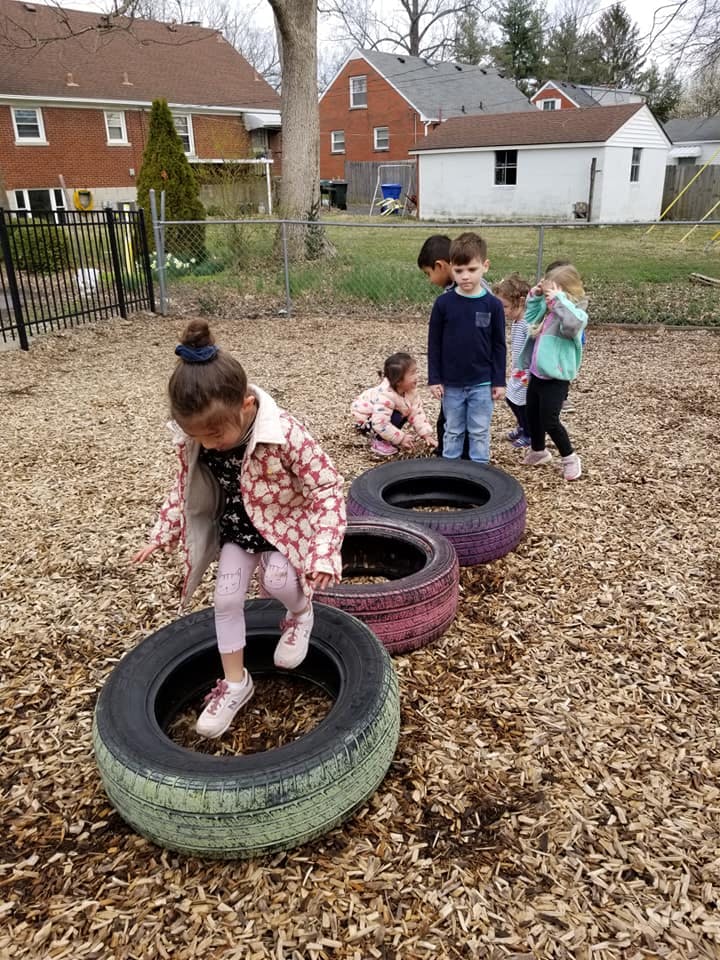 Child stepping through tires on a playground with other children