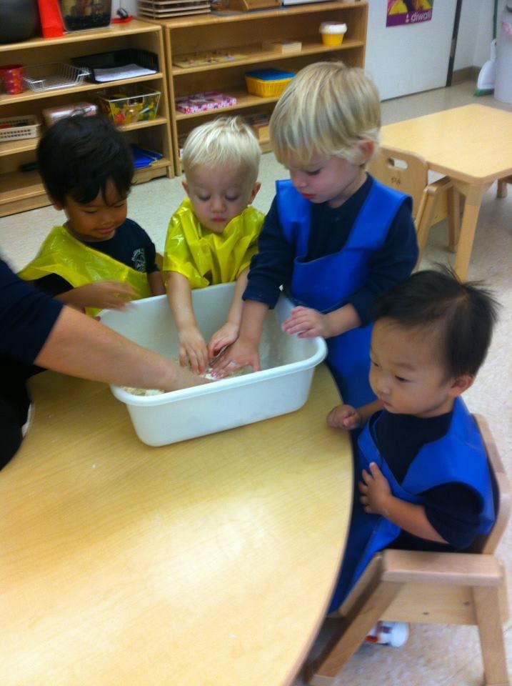 Children and an adult washing hands in a basin at a table