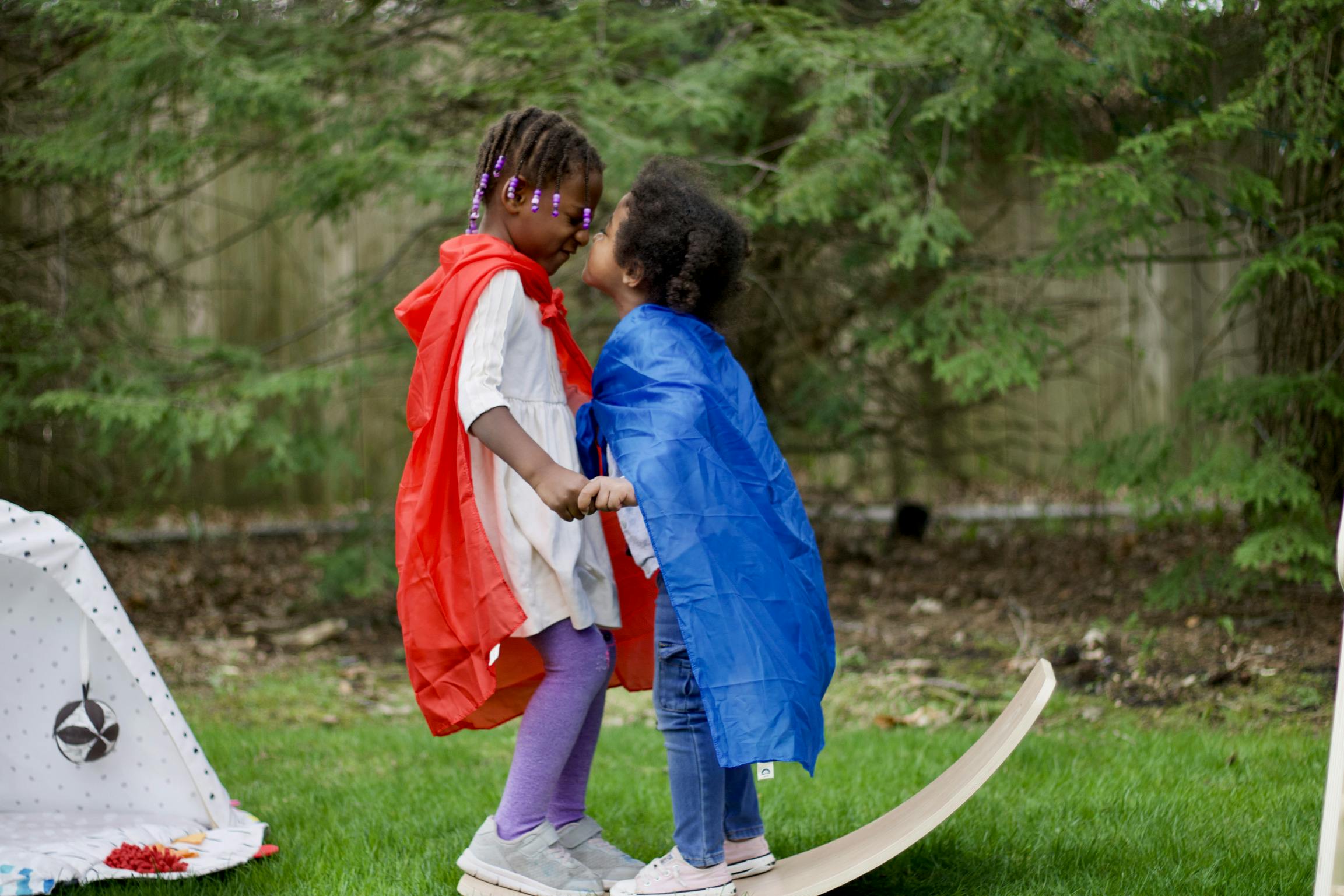 Two children in capes holding hands on a balance board