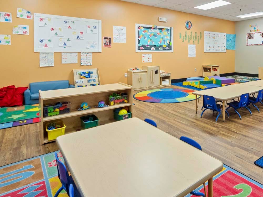 Colorful classroom with small tables and chairs, play mats, and learning materials