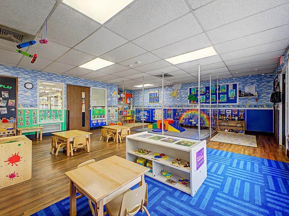 Classroom with small tables and chairs, play area, and colorful decorations
