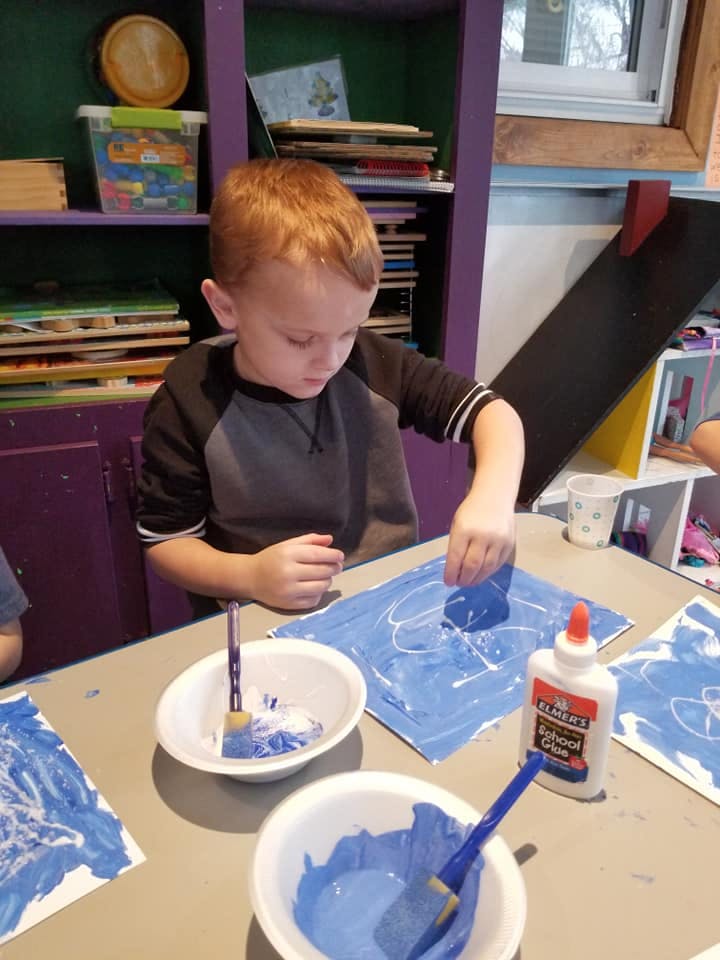 Child doing an art project with blue paint and glue