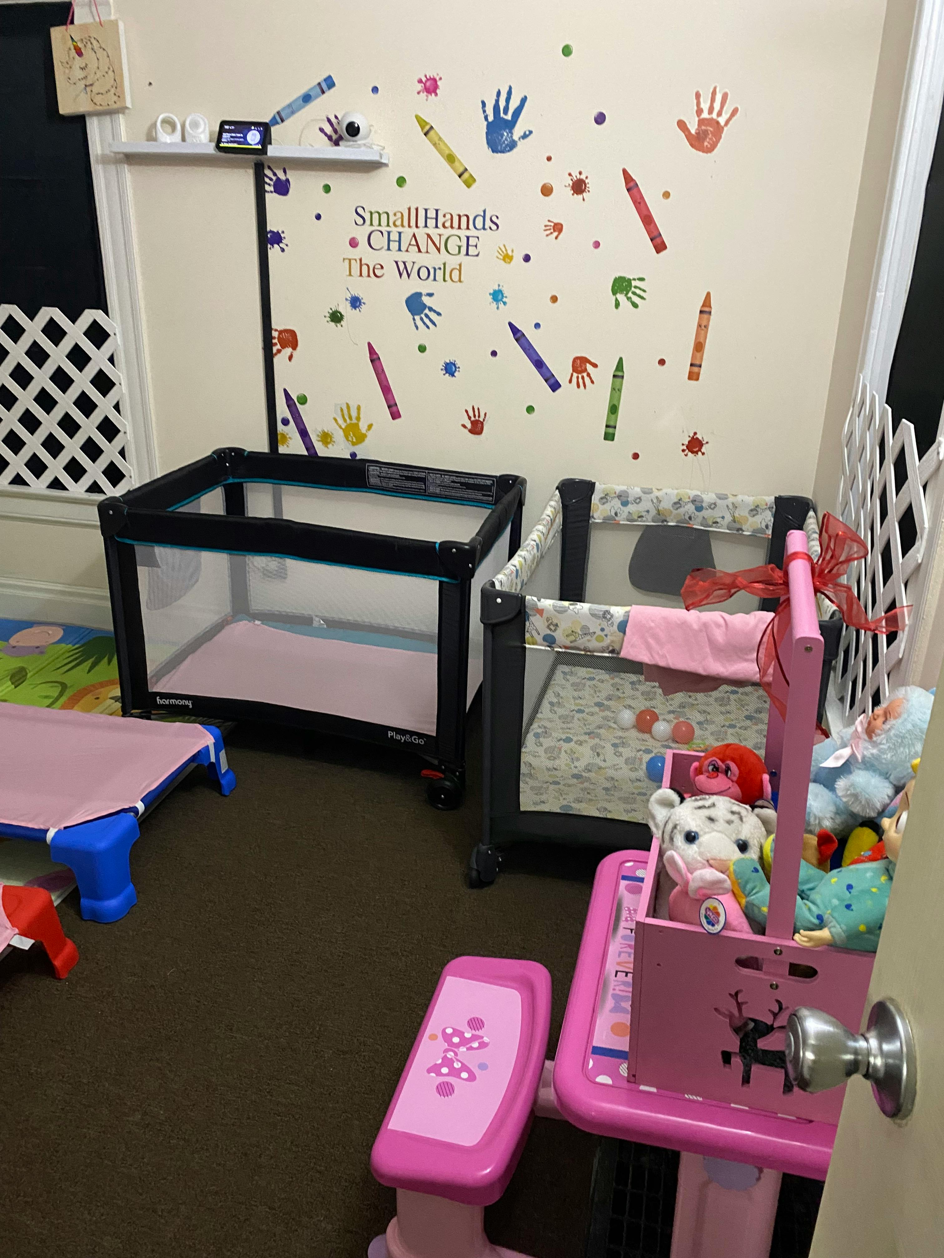 Playard and a pink toy high chair with dolls next to a wall with handprint and crayon decals