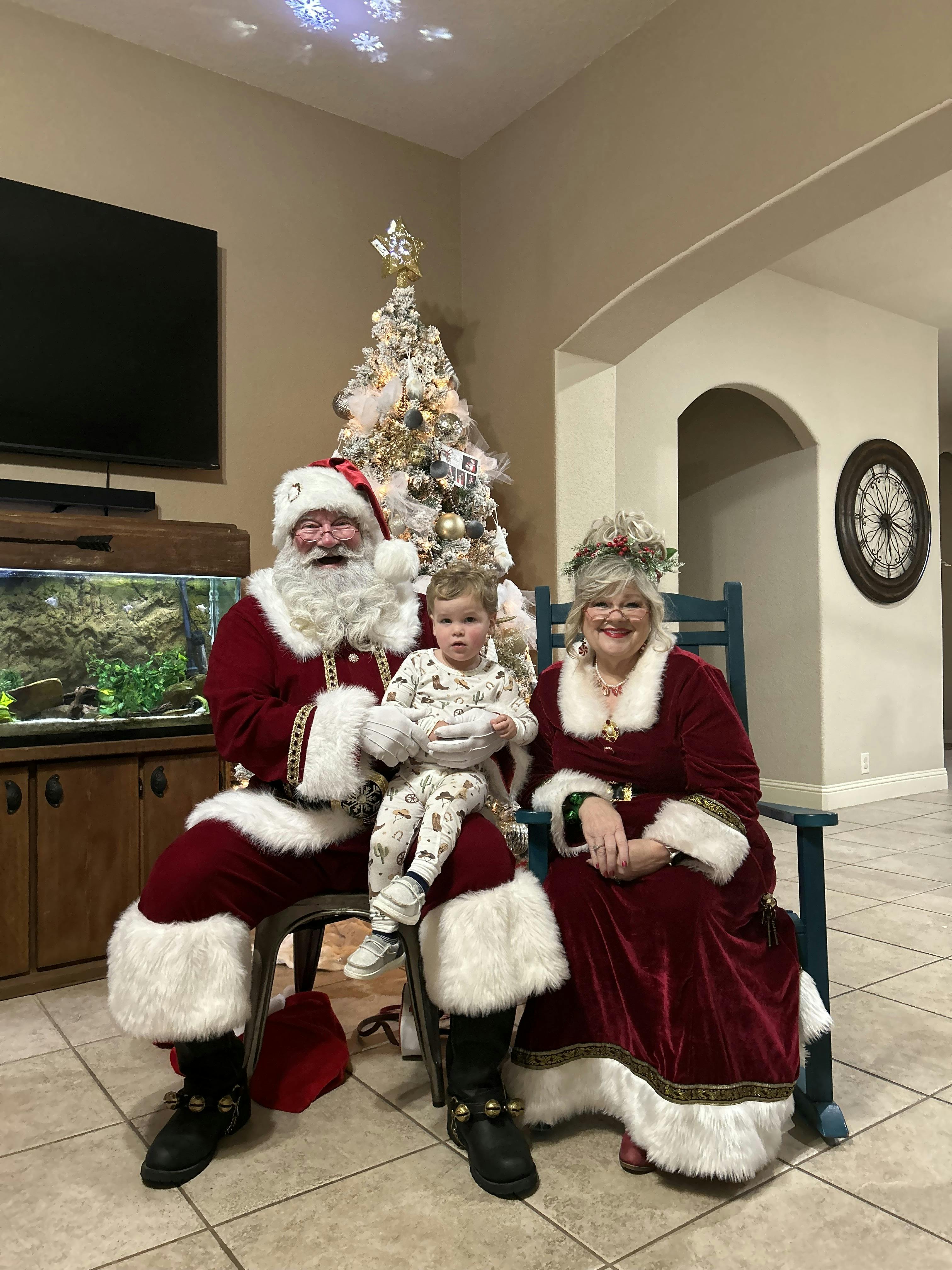 Person dressed as Santa holding a child, person dressed as Mrs Claus sitting next to them