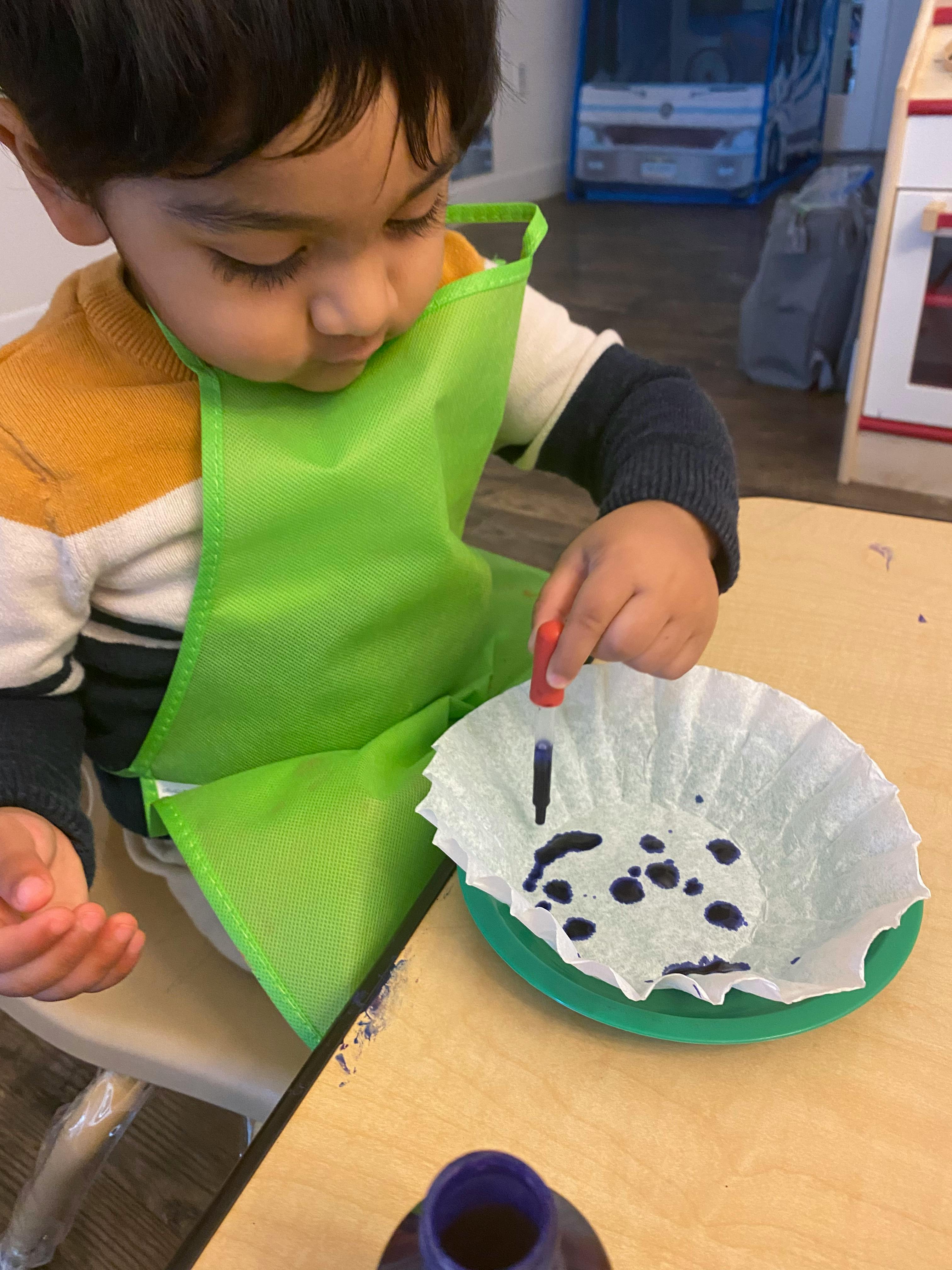 Child in a green apron using a dropper to add liquid to a coffee filter