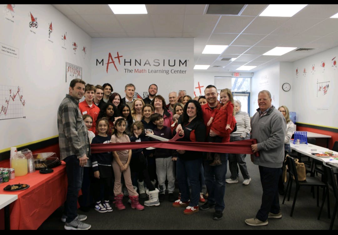 Group of people including many children at a ribbon-cutting ceremony for "Mathnasium"