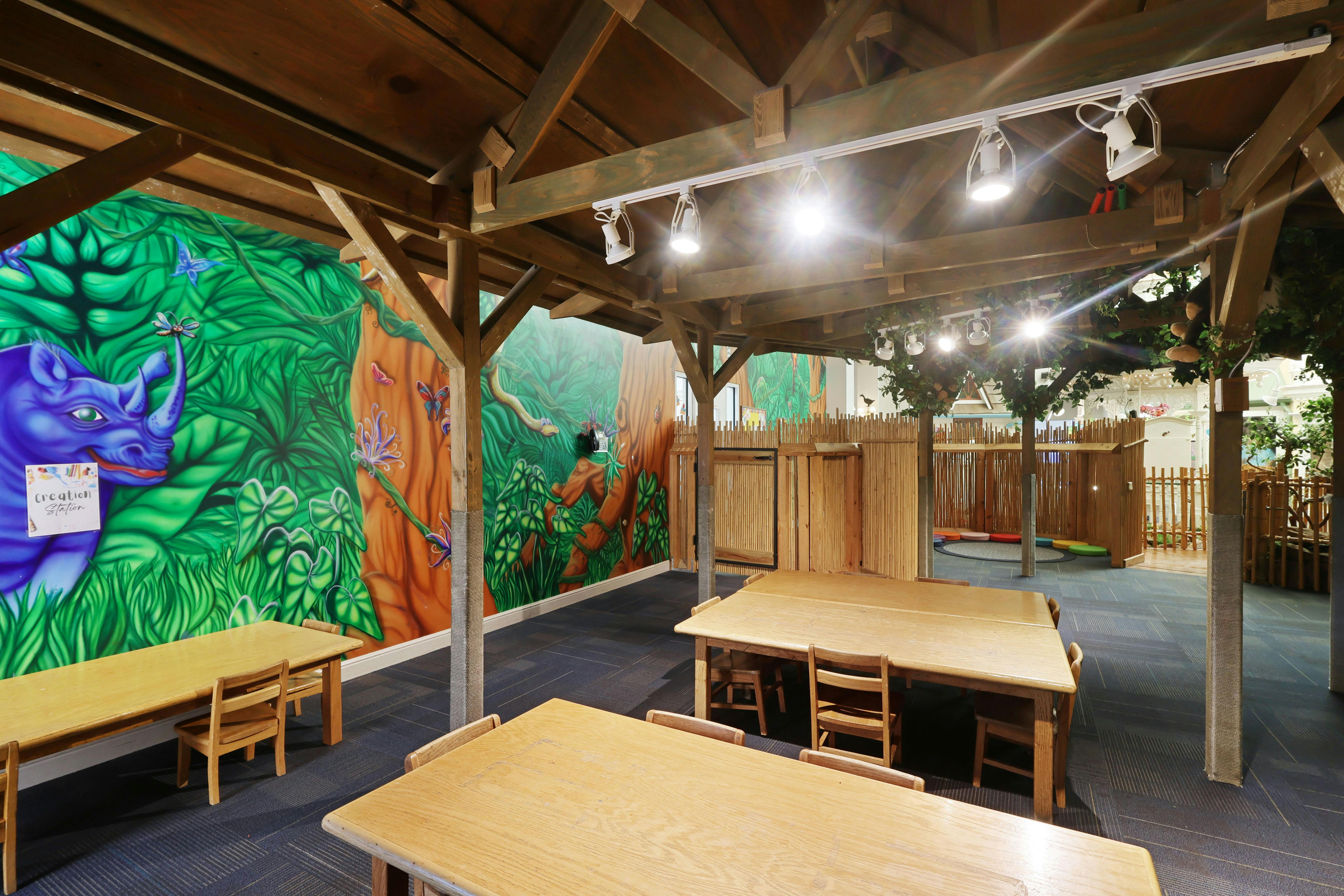 Children's play area with tables, chairs, and colorful jungle-themed murals