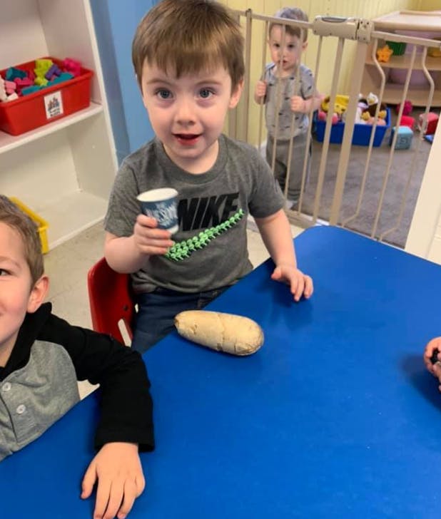Child holding a small cup at a blue table with another child